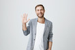 Friendly positive smiling bearded man in trendy jacket over white t-shirt and waving with his hand, hailing business partners at meeting. Good-looking businessman greets someone