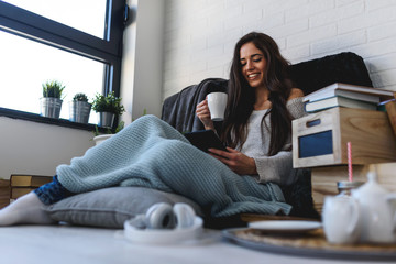 Wall Mural - Beautiful young woman at home drinking coffee reading a book