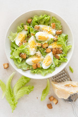 Wall Mural - Caesar salad with eggs, lettuce and parmesan cheese on plate. Top view