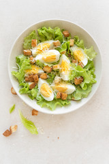 Wall Mural - Caesar salad with eggs, lettuce and parmesan cheese on plate. Top view