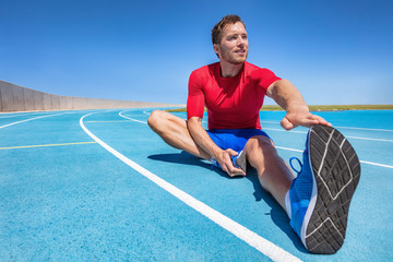 Wall Mural - Man runner stretching legs preparing for run training on outdoor stadium running tracks Male fitness sport athlete outdoors doing warm-up toe touch single leg exercise.