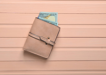 Wall Mural - A purse with dollar bills on a pink wooden table. Top view.