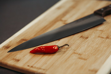 Red Chilli on the old wooden chopping board and shiny knife next to them