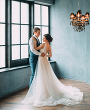 Wedding Is A Solemn Day. Stylish Young Couple Posing Against The Backdrop Of A Luxurious Interior. The Groom Hugs The Bride's Waist. Fine's Photo