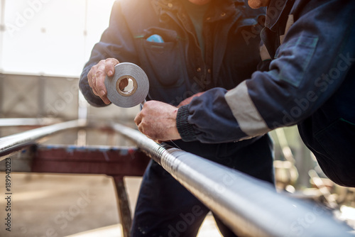Fotografía Focus hand view of professional industrial workers in uniform bonding metal pipe with duct tape