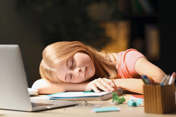 Teenage girl falling asleep while doing homework at table in evening