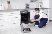 Young Man Repairing Oven In Kitchen