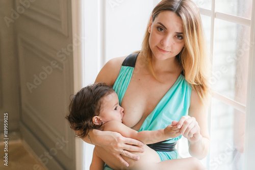 Загрузить A Mother breastfeeding her little baby girl in her arms sitting o...