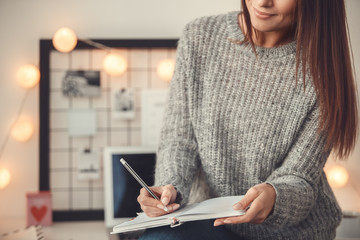 Young woman freelancer indoors home office concept winter atmosphere taking notes in planner close-up