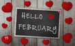 Blackboard with words hello february, surrounded by red hearts, on vintage wooden background