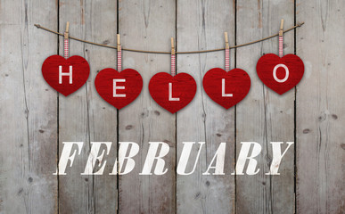 hello february written on hangingred hearts and weathered wooden background