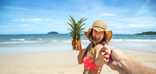 beautiful girl in swimsuit and pineapple walks on the beach holding the hand of the guy