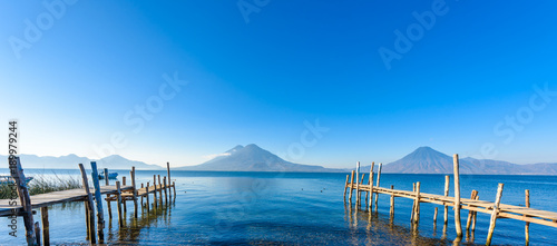 Plakat Drewniane molo nad jeziorem Atitlan na plaży w Panajachel w Gwatemali. Z piękną scenerią krajobrazową wulkanów Toliman, Atitlan i San Pedro w tle. Volcano Highland w Ameryce Środkowej.