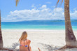 Frau sitzt im Bikini mit dem Rücken zur Kamera am weißen Sandstrand und schaut auf das Meer, Dominikanische Republik, Karibik, Samana