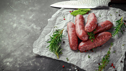 Wall Mural - Freshly made raw breed butchers sausages in skins with herbs on crumpled paper.