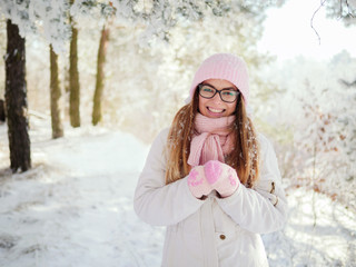 Wall Mural - Adorable happy young blonde woman in pink knitted hat scarf having fun strolling snowy winter forest in nature