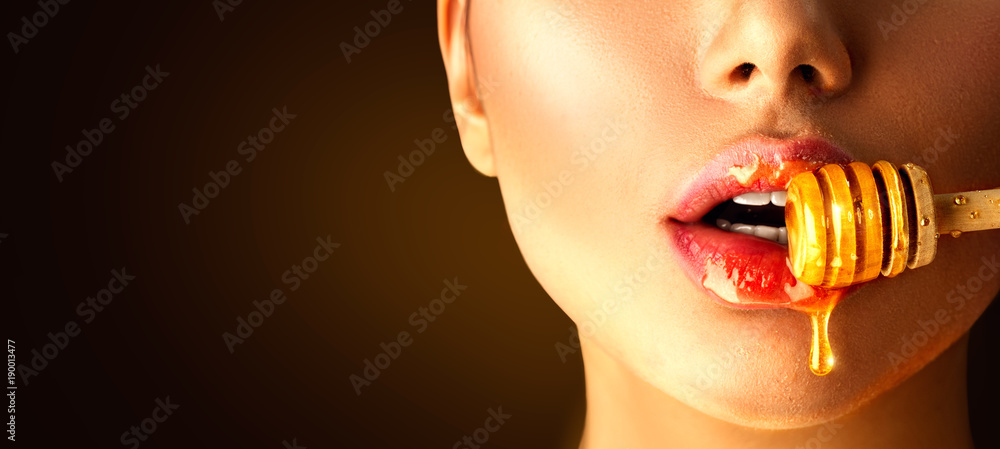 Honey dripping on sexy girl lips from the wooden spoon. Beauty model woman eating honey - obrazy, fototapety, plakaty 