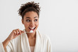 © Yakobchuk Olena - Portrait of smiling girl brushing teeth. She is wearing housecoat and looking aside with happiness. Copy space in right side. Isolated on background