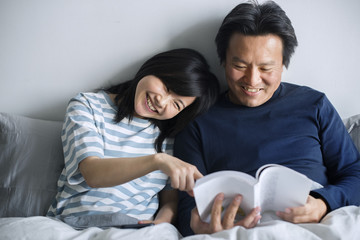 Poster - Asian couple reading a book on bed together