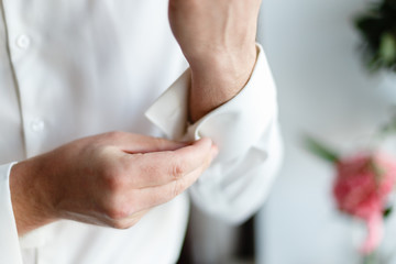 Wall Mural - A man wears buttons of cufflinks on the sleeves of the white shirt. Businessman getting dressed by the window.