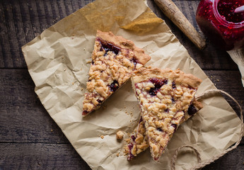 Wall Mural - Homemade tasty shortcrust raspberry pie with crumble on kraft paper on old wooden table background. Jam Tart Pieces Snack Food. Top view