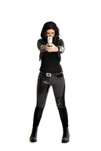 Full Length Portrait Of Black Haired Girl Wearing Leather Outfit. Standing Pose While Holding A Gun, Isolated On A White Studio Background.