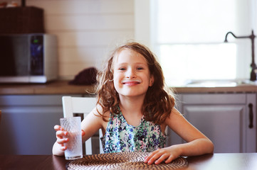 happy 8 years old child girl having breakfast in country kitchen, drinking milk and eating toast with strawberry