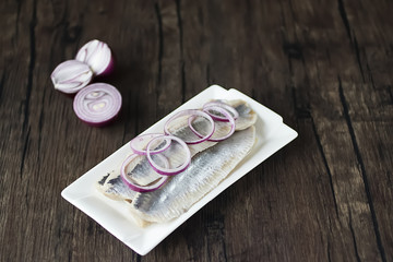 Herring fillets in a white plate on a dark wooden table.