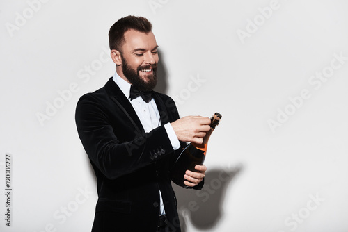 Foto  Let us celebrate! Handsome young man in full suit opening a bottle of champagne