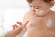 © Africa Studio - Woman applying body cream on her baby against light background