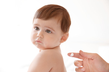 Wall Mural - Woman applying body cream on her baby against light background