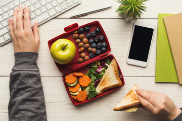 Wall Mural - Woman eating healthy sandwich from lunch box at her working table