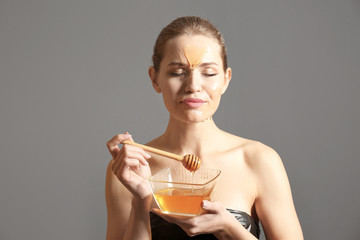 Canvas Print - Young woman with honey on her face against grey background. Skin treatment