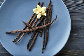 Wall Mural - Plate with vanilla sticks and flower on wooden background