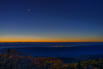 Morning dark sunrise with blue sky and golden yellow orange autumn foliage in Dolly Sods, Bear Rocks, West Virginia with overlook of mountain valley, stars, moon, and Jupiter, Venus, Mars planets