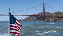 View Towards The Northern Tower Of Golden Gate Bridge, With An American Flag In The Foreground Waving In The Wind, From A Ferryboat Connecting Sausalito To San Francisco, California, USA