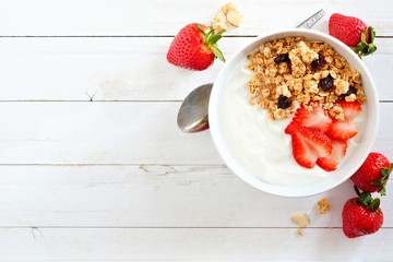 Wall Mural - bowl of yogurt with strawberries and granola, over a white wood background. flat lay, side orientati