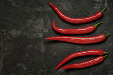 Group Of Five Chilly Peppers On A Black Textured Rustic Cement Background, Top View With Copy Space For Your Text