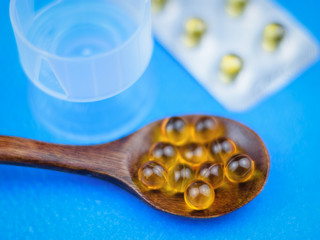 Wall Mural - Fish oil capsules in a dark wooden spoon and a blister on a blue table. Traditional medicine.