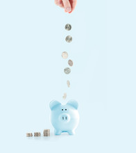 Female Hand Putting Coin Into Piggy Bank On Pastel Blue Background