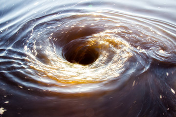 a small swirling circular motion of a water whirlpool with sunlight bouncing off water