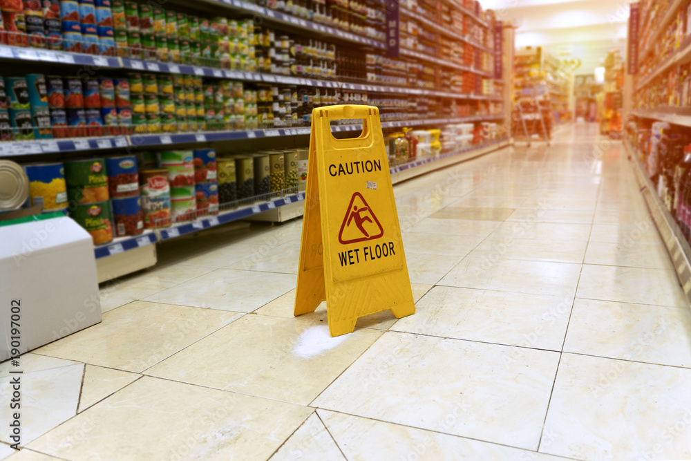Yellow sign - caution. Wet floor is in the supermarket against the background of blurry products standing on the shelves - obrazy, fototapety, plakaty 