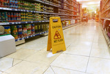 Fototapeta Tulipany - Yellow sign - caution. Wet floor is in the supermarket against the background of blurry products standing on the shelves