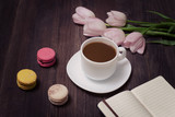 Fototapeta Tulipany - Cup of tea, macarons, pink tulips and notebook on wooden background.