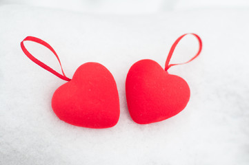 Two red hearts with ribbons laying on white snow on winter day