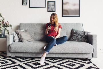 Young woman at home sitting on the couch using smartphone