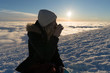 Girl drinking tea on snow in Slovak mountains above clouds during sunset in winter