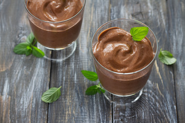 Two glasses with delicious vegan chocolate mousse made of banana with cocoa and mint on a wooden table, selective focus