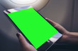 © Farknot Architect - Mockup image of a woman holding and looking at black tablet pc with blank green desktop screen next to an airplane window