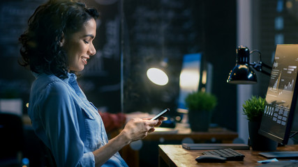 Wall Mural - beautiful female financier uses mobile phone, writing messages, emails while smiling. in the backgro